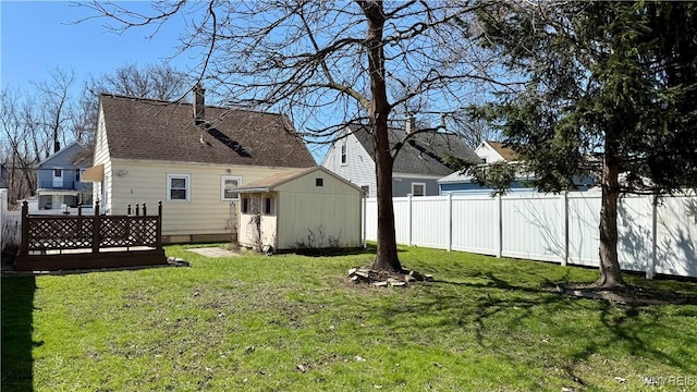 back of house with a yard, fence, an outbuilding, roof with shingles, and a shed