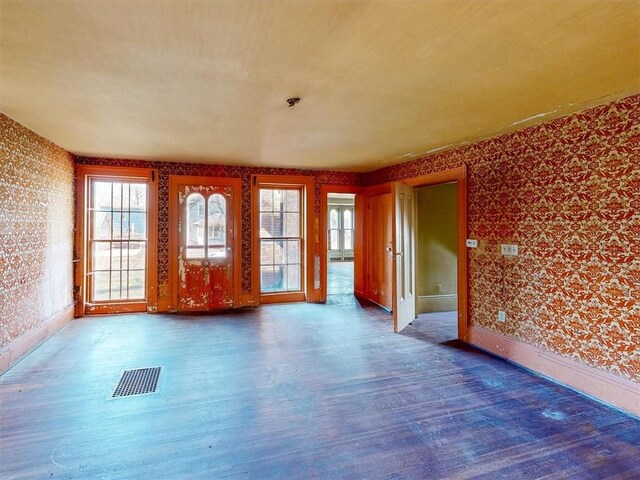 unfurnished room with visible vents, wallpapered walls, wood finished floors, and plenty of natural light
