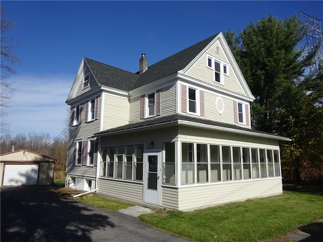 view of side of home featuring a chimney, a sunroom, an outdoor structure, aphalt driveway, and a shingled roof