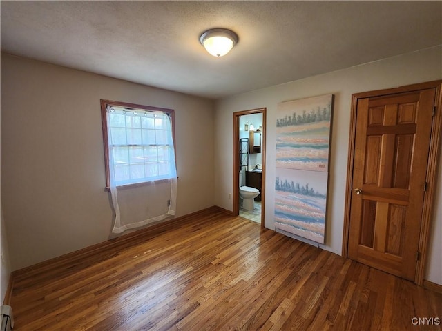 interior space featuring wood finished floors, a baseboard heating unit, and baseboards