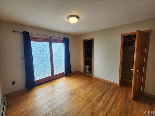 unfurnished bedroom featuring light wood-style floors, a closet, baseboard heating, ensuite bathroom, and baseboards