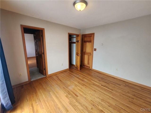 unfurnished bedroom with light wood finished floors, a closet, ensuite bath, and baseboards