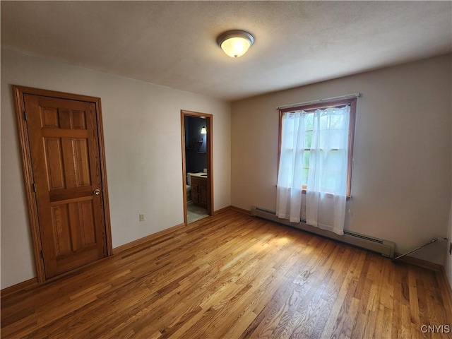 unfurnished room with a baseboard heating unit, wood finished floors, and baseboards
