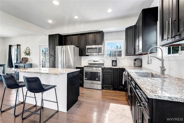kitchen featuring a kitchen island, a sink, dark cabinets, a breakfast bar, and stainless steel appliances