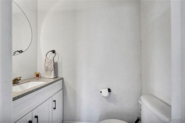 half bath featuring vanity, a textured wall, and toilet