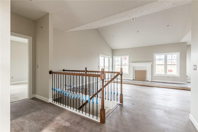 hall with baseboards, an upstairs landing, wood finished floors, and high vaulted ceiling