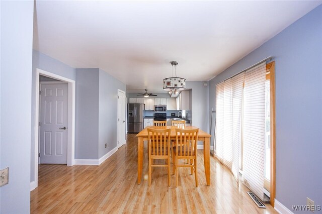 dining room with baseboards, visible vents, ceiling fan with notable chandelier, and light wood finished floors