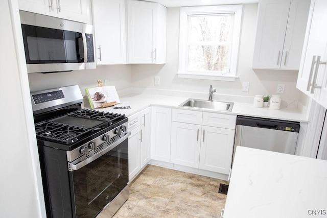 kitchen featuring a sink, white cabinets, stainless steel appliances, and stone finish flooring