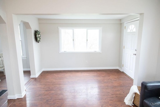 unfurnished living room featuring dark wood-type flooring, arched walkways, and baseboards