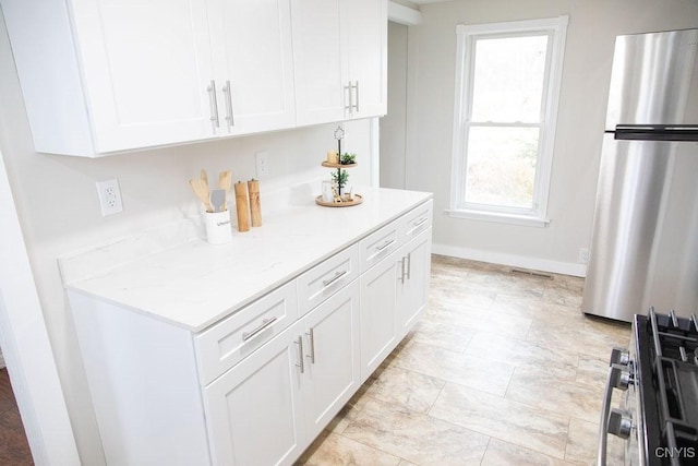 kitchen featuring light stone countertops, visible vents, white cabinetry, baseboards, and freestanding refrigerator