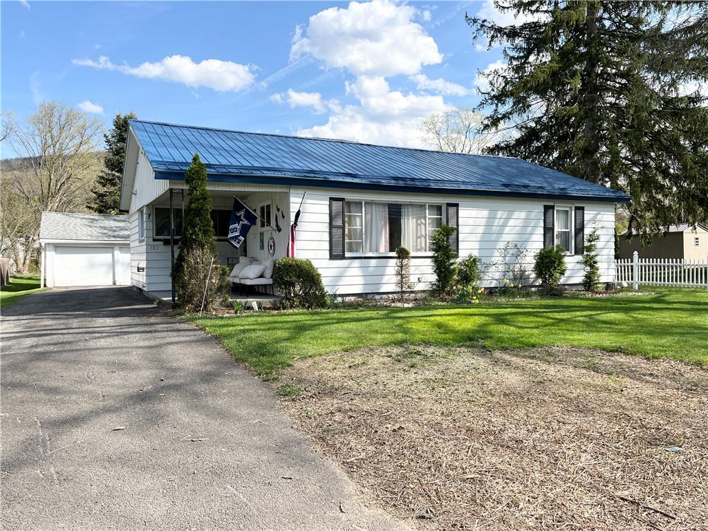 single story home featuring a detached garage, fence, a front yard, and metal roof