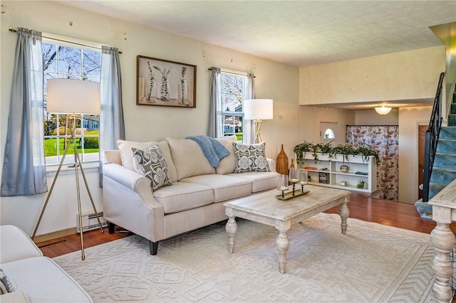 living area featuring baseboard heating, wood finished floors, and stairs