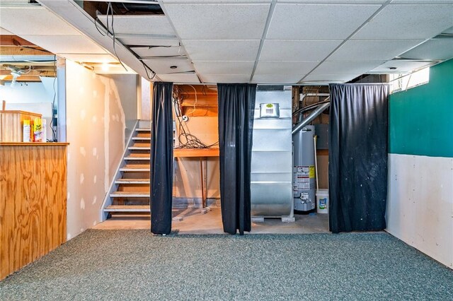 below grade area featuring stairs, gas water heater, carpet flooring, and a paneled ceiling
