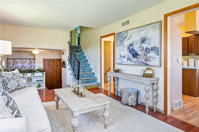 living room with stairs, visible vents, and wood finished floors