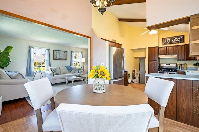 dining room featuring light wood finished floors, high vaulted ceiling, and beam ceiling
