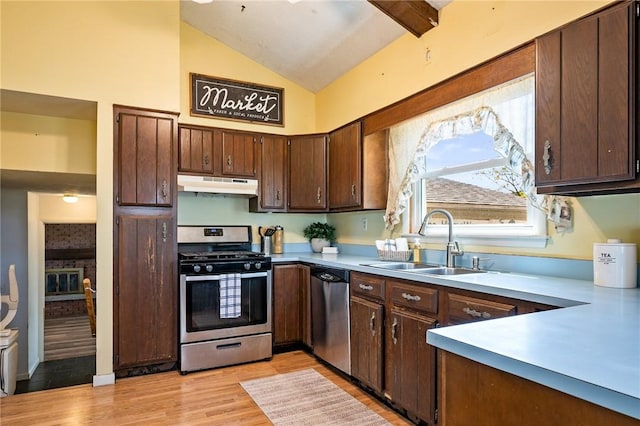 kitchen with a sink, stainless steel appliances, under cabinet range hood, light countertops, and lofted ceiling