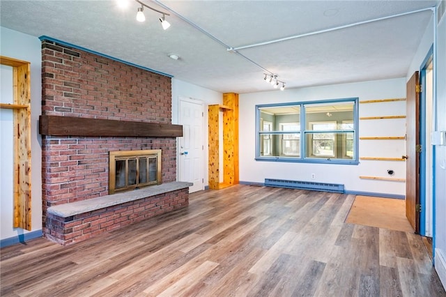 unfurnished living room featuring a baseboard heating unit, a brick fireplace, rail lighting, and wood finished floors