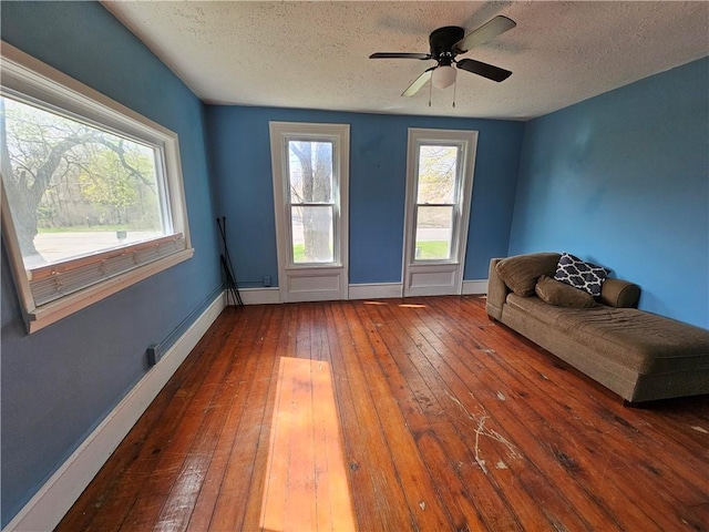 unfurnished living room featuring a textured ceiling, ceiling fan, hardwood / wood-style floors, and baseboards