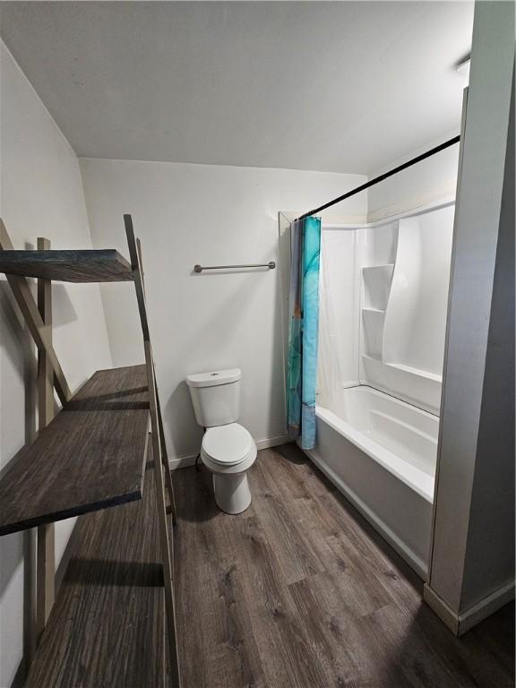 bathroom with shower / bath combo with shower curtain, baseboards, wood finished floors, and toilet