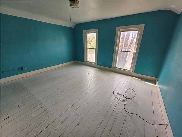 empty room with vaulted ceiling, hardwood / wood-style flooring, and baseboards