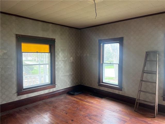 empty room with baseboards, visible vents, ornamental molding, and hardwood / wood-style flooring