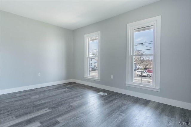 spare room with dark wood-style flooring, baseboards, and plenty of natural light