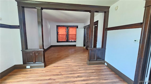corridor featuring ornate columns, wood finished floors, and baseboards