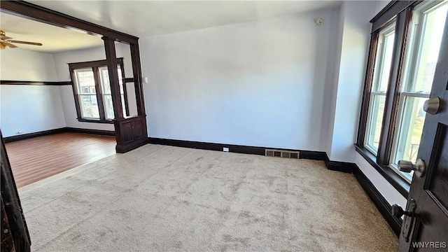 carpeted spare room featuring ceiling fan, plenty of natural light, visible vents, and baseboards