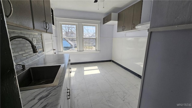kitchen featuring a sink, baseboards, under cabinet range hood, a fireplace, and marble finish floor
