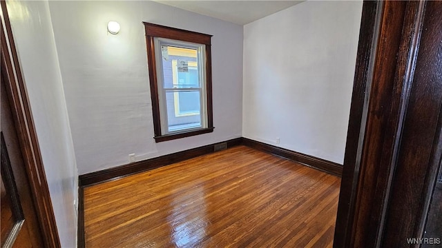 spare room featuring baseboards and dark wood-type flooring