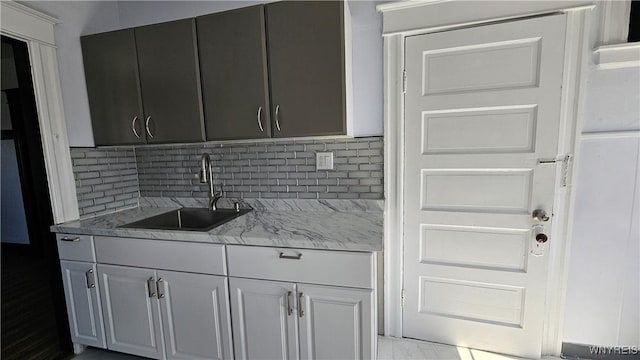 kitchen with tasteful backsplash, light stone countertops, and a sink