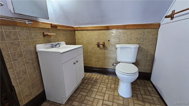 bathroom featuring tile walls, toilet, brick patterned floor, and vanity