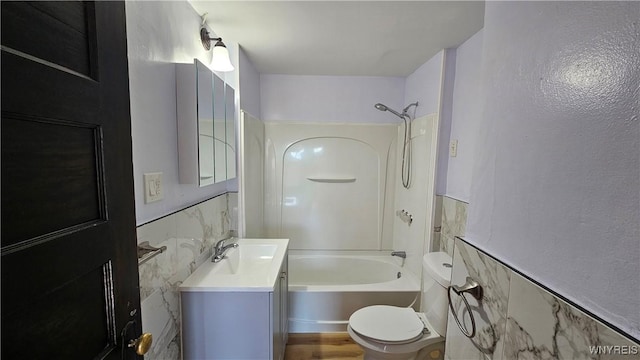 bathroom featuring bathing tub / shower combination, tile walls, a wainscoted wall, toilet, and vanity