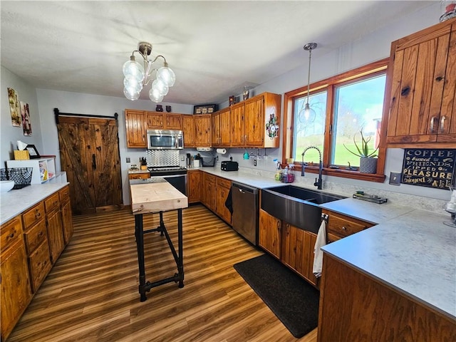 kitchen featuring brown cabinets, a sink, stainless steel appliances, dark wood-style floors, and hanging light fixtures