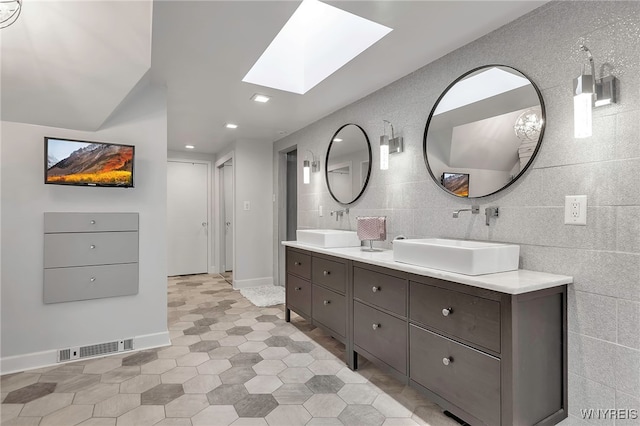 bathroom with visible vents, a skylight, double vanity, and a sink