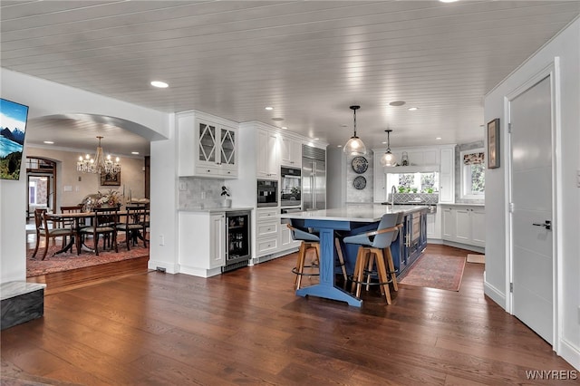 kitchen with light countertops, arched walkways, white cabinetry, and beverage cooler