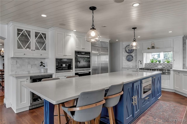 kitchen featuring blue cabinetry, built in appliances, a sink, white cabinetry, and wine cooler
