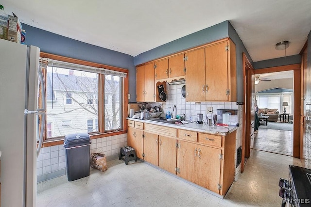 kitchen with decorative backsplash, a sink, ceiling fan, light countertops, and freestanding refrigerator