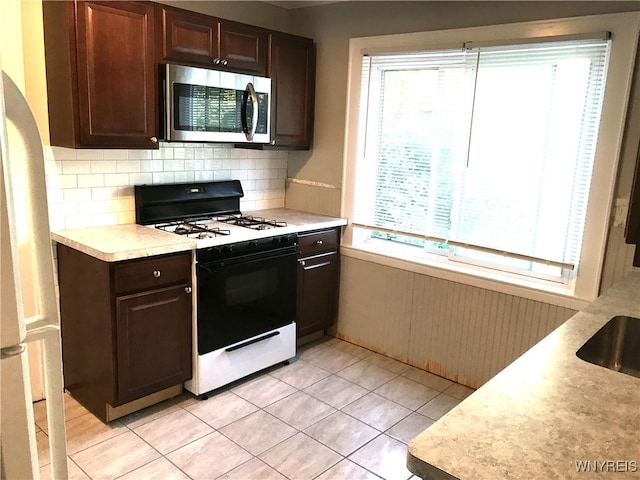 kitchen with stainless steel microwave, dark brown cabinetry, range with gas cooktop, backsplash, and light countertops