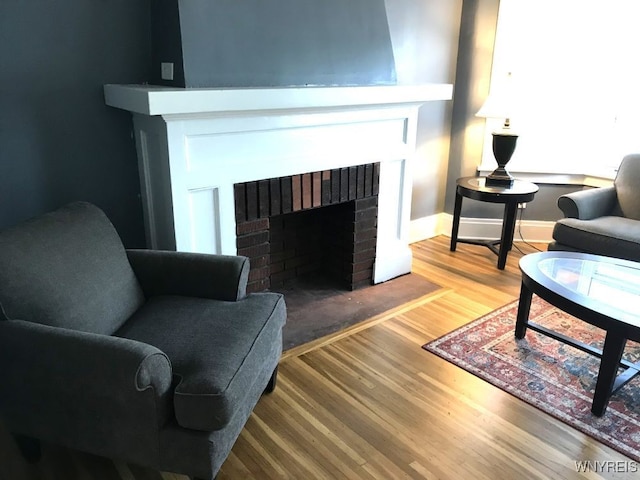living area featuring baseboards, wood finished floors, and a brick fireplace