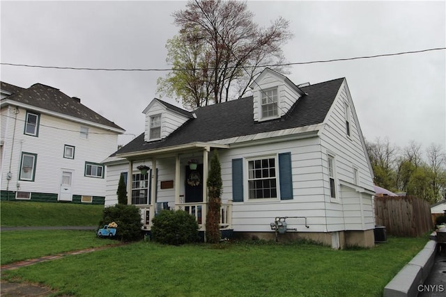 new england style home with fence, covered porch, a front yard, a shingled roof, and central air condition unit
