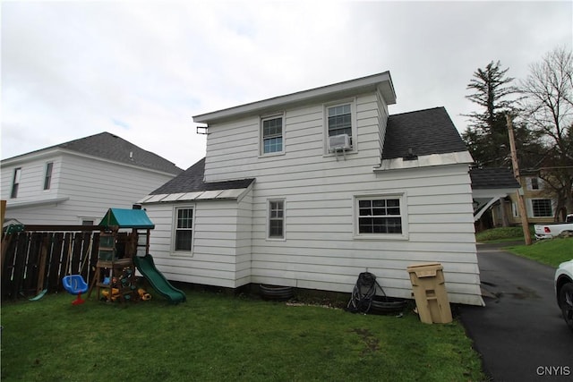 rear view of house featuring roof with shingles, a lawn, a playground, and cooling unit