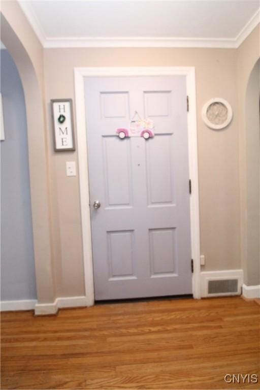 doorway featuring visible vents, ornamental molding, baseboards, arched walkways, and light wood-style flooring