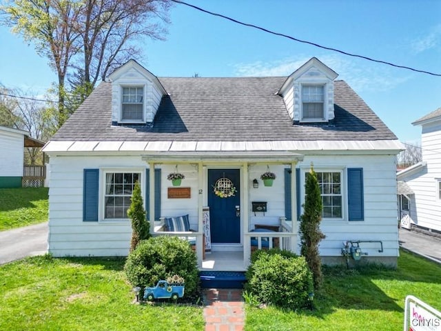cape cod-style house featuring a porch, a front lawn, and roof with shingles