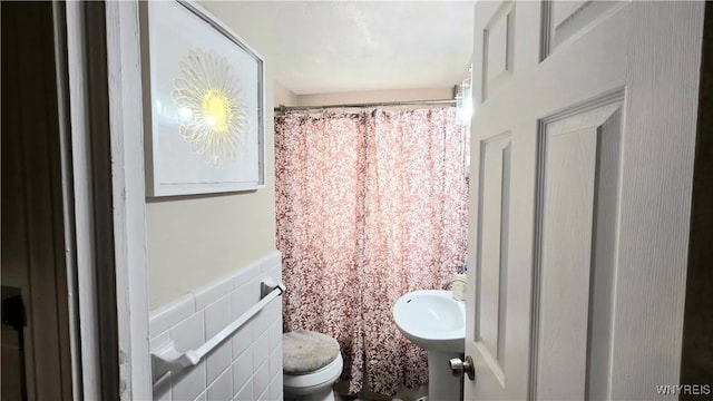 full bath with tile walls, curtained shower, toilet, and a sink