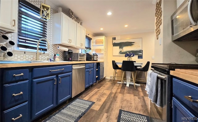 kitchen featuring appliances with stainless steel finishes, dark wood-type flooring, white cabinetry, blue cabinets, and butcher block counters