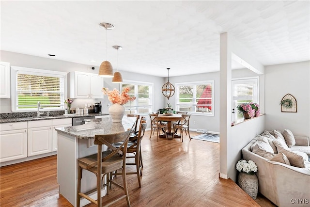 kitchen with light stone countertops, stainless steel dishwasher, white cabinets, a sink, and a kitchen breakfast bar