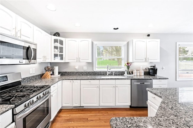kitchen with dark stone countertops, light wood-type flooring, stainless steel appliances, and a sink