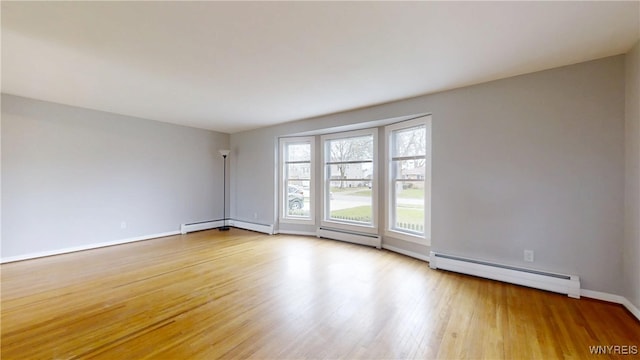 unfurnished room featuring wood finished floors, a baseboard heating unit, and baseboards