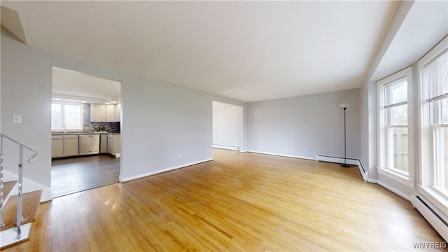 unfurnished living room featuring a baseboard heating unit, light wood finished floors, stairs, and a baseboard radiator